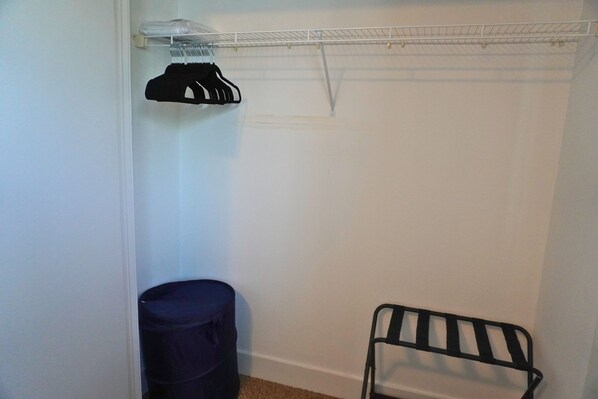 A closet with a hanging rack, a storage bin, and a chair.