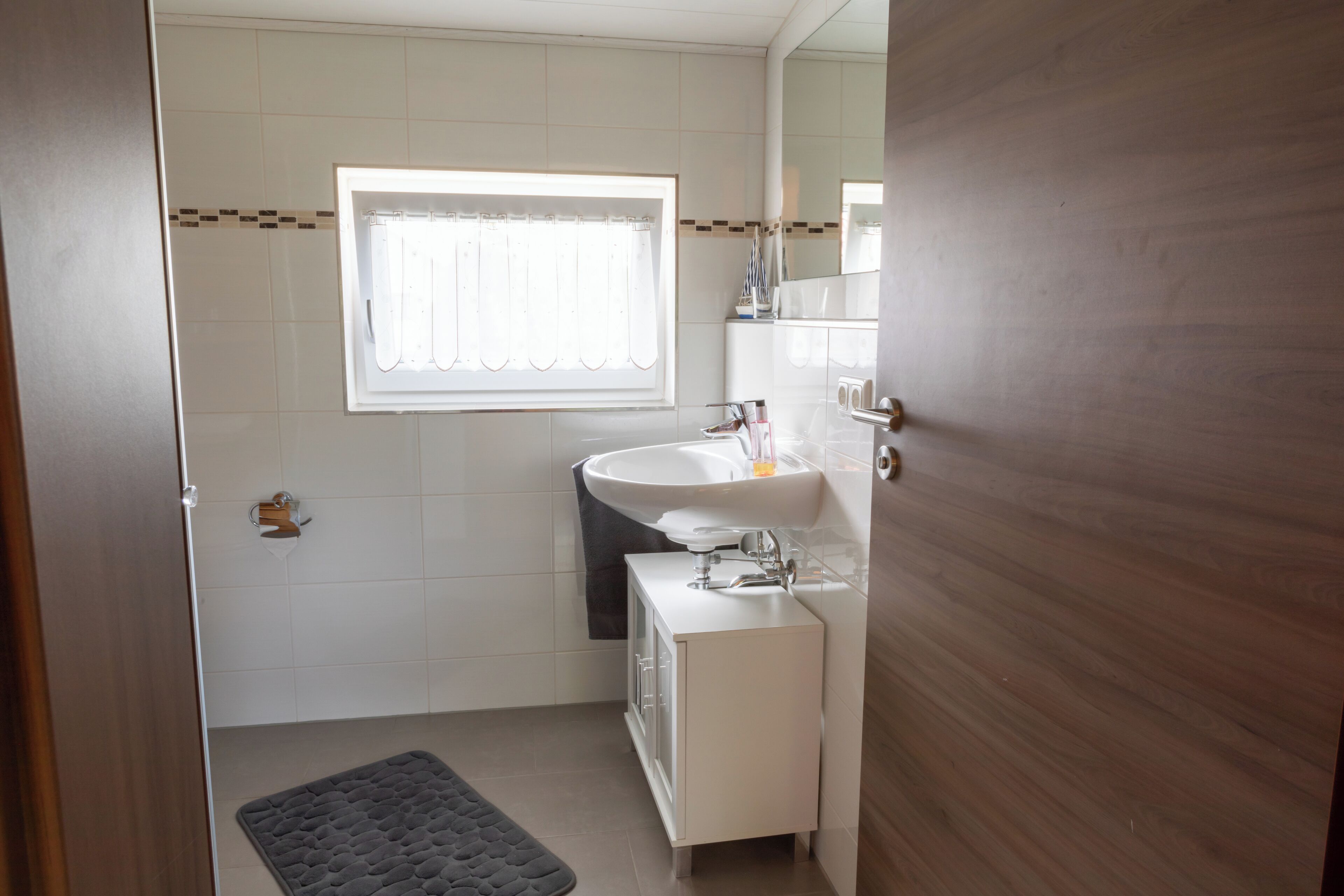 A bathroom with a window, a sink, a mirror, and a door.