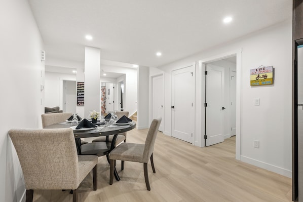 A modern dining area with a round table, four chairs, and a decorative wall sign. - Lake Community Hideout (Chestermere)