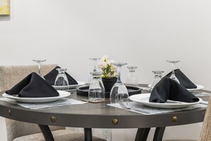 A round dining table with plates, folded napkins, and clear glassware. - Lake Community Hideout (Chestermere)