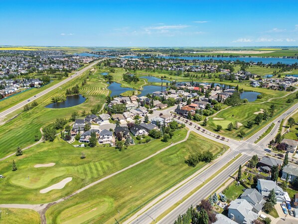 An aerial view of a residential area with houses, roads, and a golf course. - Lake Community Hideout (Chestermere)