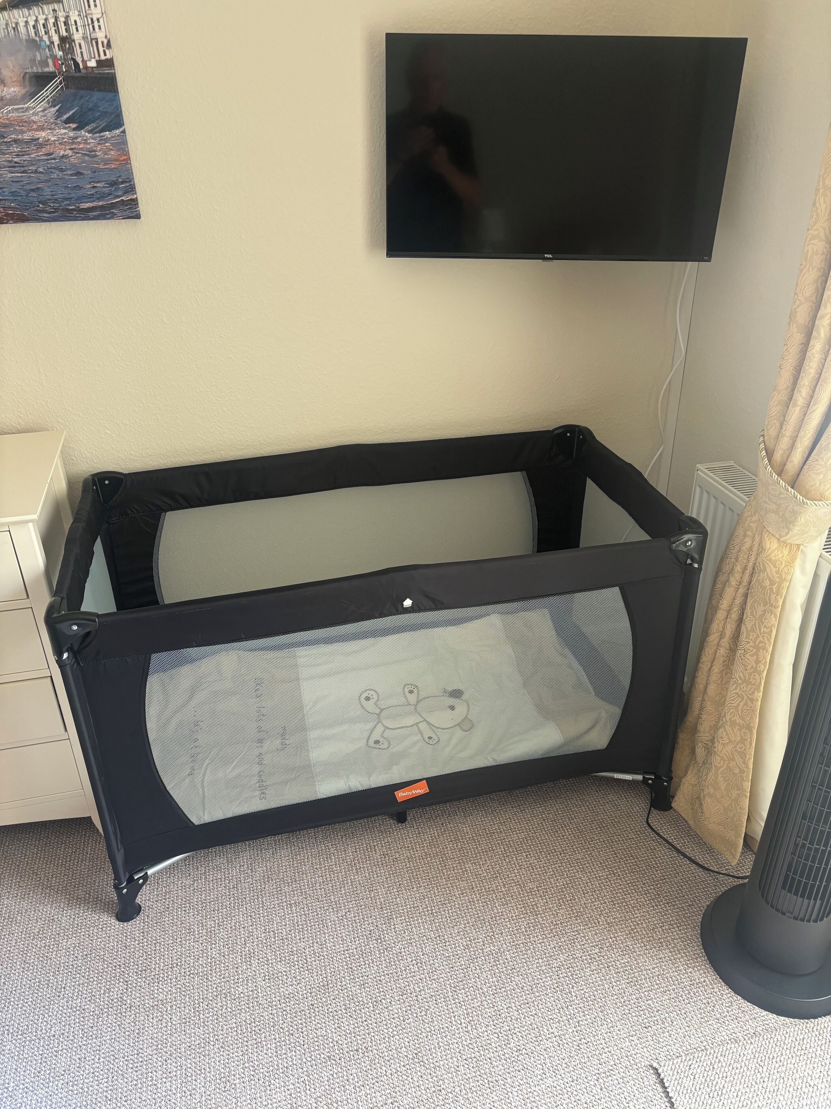 A room with a black baby playpen, a television on the wall, and a radiator.