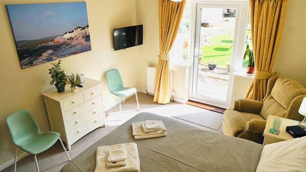 Habitación de hotel con cama, escritorio, silla, televisión y vista al jardín por la ventana.