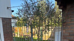 Une entrée fermée par un portail, agrémentée d’un arbre en pot, d’un mur de briques et d’une grille en métal.