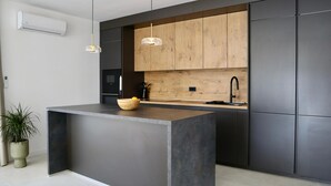 Une cuisine moderne dotée d’un îlot central, de meubles de couleur sombre, d’un pare-feu en bois et de luminaires suspendus.