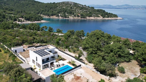 Une maison moderne avec une piscine, entourée d’une végétation luxuriante et offrant une vue sur la mer.