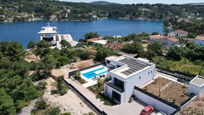 Une maison moderne dotée d’une piscine, de panneaux solaires et offrant une vue sur un lac et des collines.
