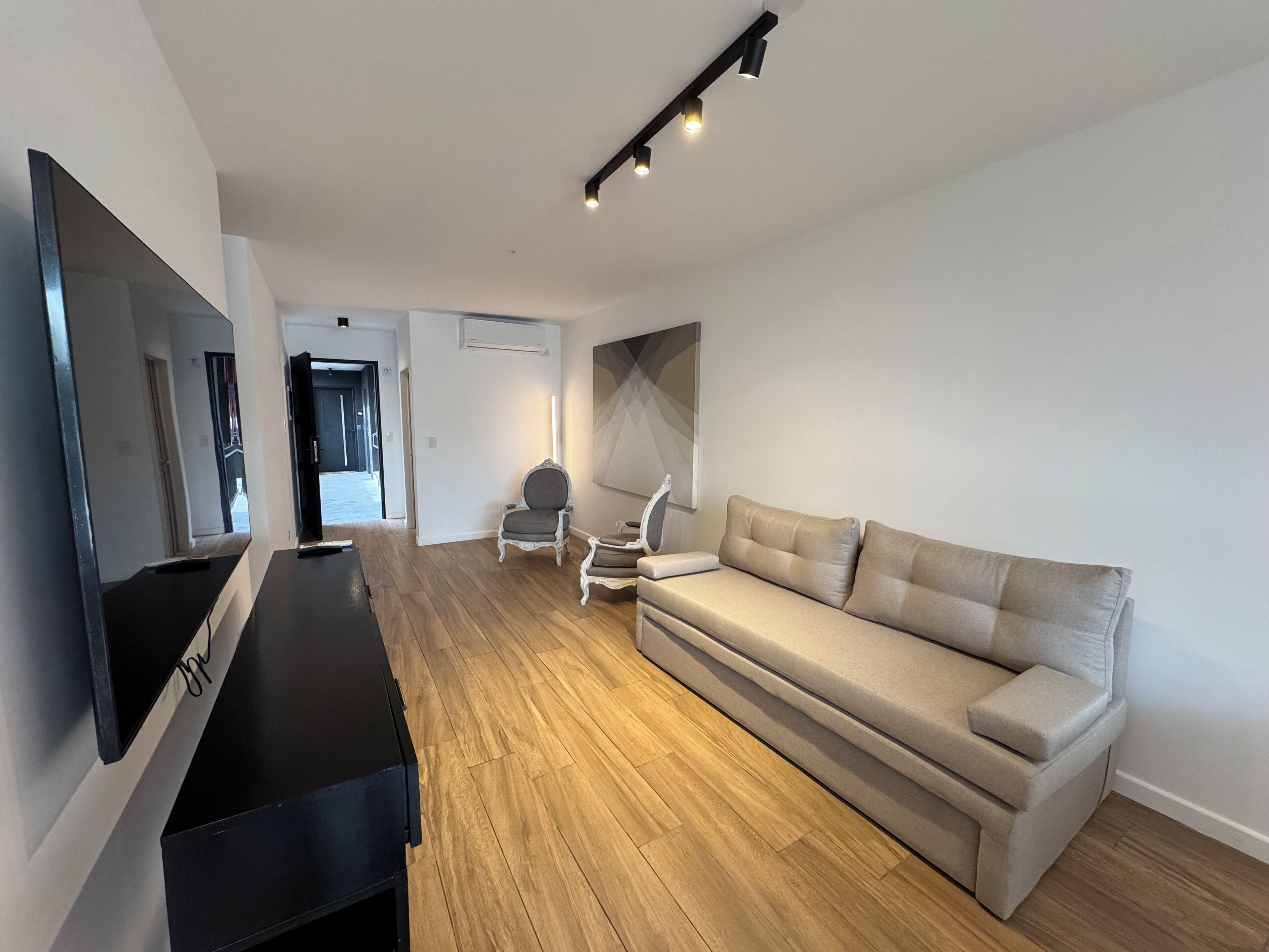 Una sala de estar moderna con un televisor de pantalla plana, un sofá, una silla y piso de madera.