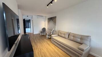 Una sala de estar moderna con un televisor de pantalla plana, un sofá, una silla y piso de madera.