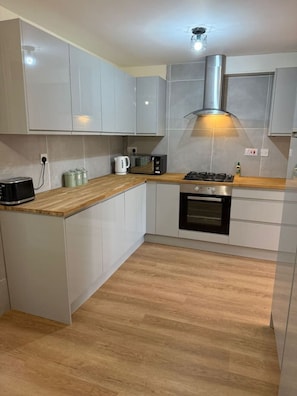 A compact kitchen with white cabinets, a wooden countertop, a built-in oven, and a stainless steel range hood. - 3 bed house by mustang escapes (Bradley Stoke)