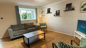 Ein Wohnzimmer mit grauem Sofa, einem gestreiften Sessel, einem Couchtisch und einem Fernseher auf einem weißen Schrank.