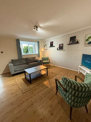 A living room with a grey sofa, a striped armchair, a coffee table, and a TV on a white stand. - 3 bed house by mustang escapes (Bradley Stoke)