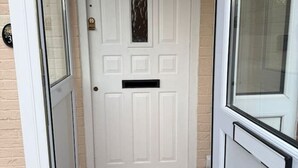 Eine weiße Tür mit der Nummer 38 darüber, ein kleines Fenster und eine Fußmatte am Eingang.