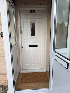 A white door with the number 38 above it, a small window, and a welcome mat at the entrance. - 3 bed house by mustang escapes (Bradley Stoke)