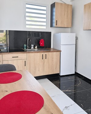 A modern kitchen with a black countertop, white cabinets, and a white refrigerator. - Ti Hibiscus  (Sainte-Rose)
