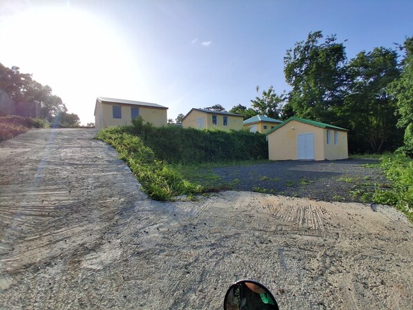 A dirt road leading to a row of yellow buildings with green roofs, surrounded by greenery.