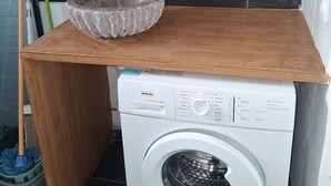 A bathroom with a wooden vanity, a round mirror, a sink, and a front-loading washing machine. - Golden Papaya  (Sainte-Rose)