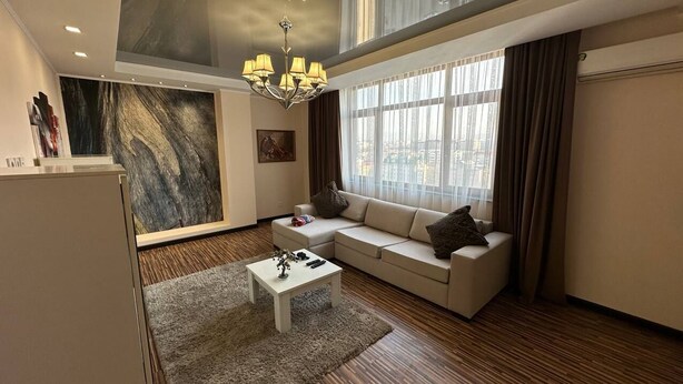 A modern living room with a sofa, a coffee table, a chandelier, and a large abstract painting on the wall.