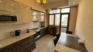 A modern kitchen with a built-in oven, microwave, and sink. There is a dining table with chairs and a window with curtains.