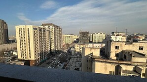 A cityscape with multiple high-rise buildings, a busy street with parked cars, and a clear sky.