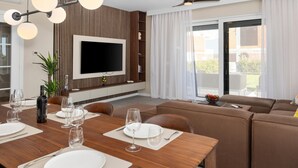 Una sala de estar moderna con comedor, un televisor de pantalla plana montado en una pared de madera y un amplio ventanal corredero que da a un espacio exterior.