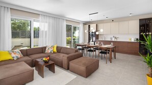 Una sala moderna con un sofá modular marrón, una mesa de comedor con sillas y una zona de cocina con encimera y armarios.