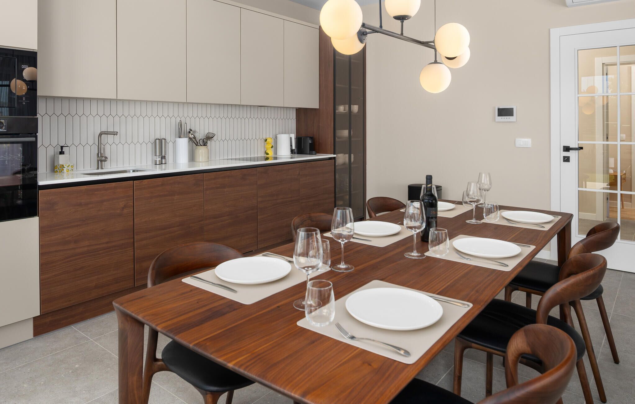A modern kitchen with a wooden dining table set for six, equipped with wine glasses and plates.