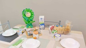 Ett dukat matbord med tallrikar, bestick och olika matvaror, inklusive förpackade snacks och en dekorativ blomsterdekoration i mitten.