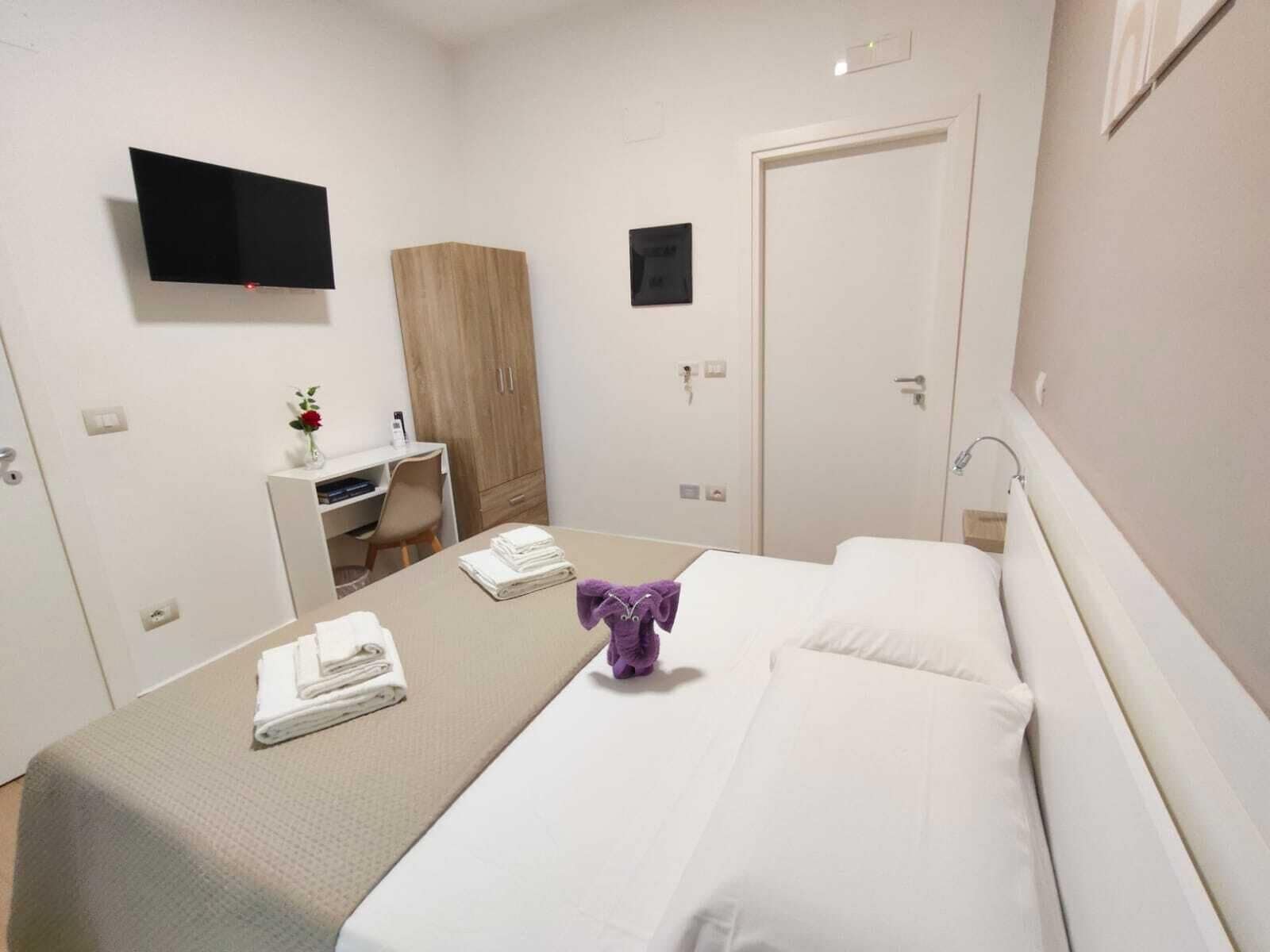 A hotel room with a bed, a desk, a wardrobe, and a TV on the wall.