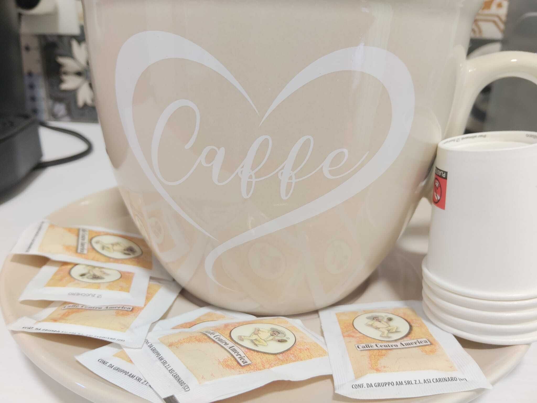 A large mug with a heart-shaped design and the word "Caffe" on it, accompanied by several smaller mugs and coffee packets.