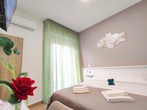 Une chambre d’hôtel avec un lit, un climatiseur fixé au mur, une fenêtre avec des rideaux verts et un tableau représentant des fleurs accroché au mur.