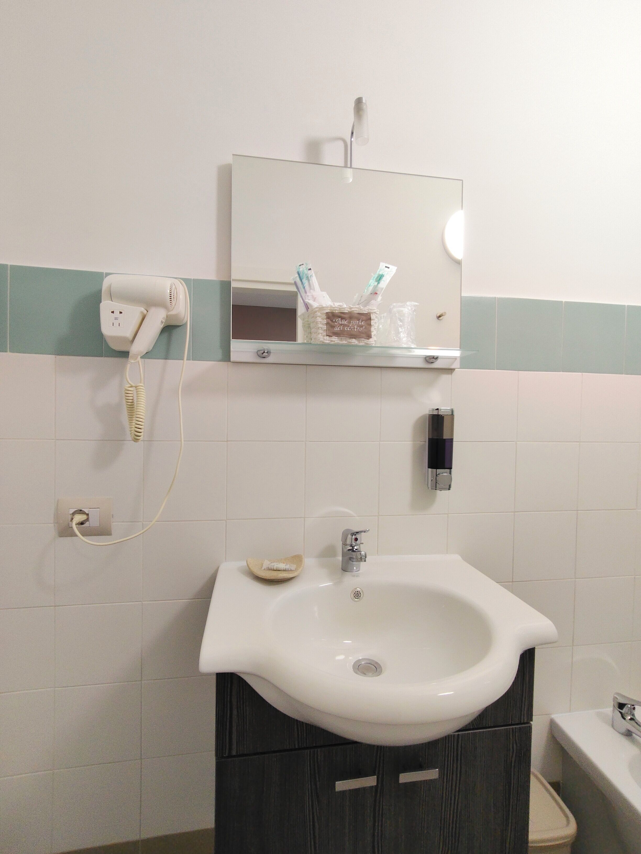 Un baño con un lavamanos blanco, un mueble de madera oscura, un secador de pelo en la pared y un espejo sobre el lavamanos.