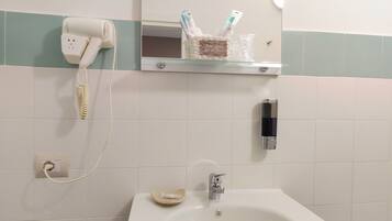 Un baño con un lavamanos blanco, un mueble de madera oscura, un secador de pelo en la pared y un espejo sobre el lavamanos.