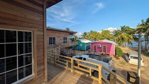 Een houten terras met uitzicht op kleurrijke bungalows en een nabijgelegen voertuig.