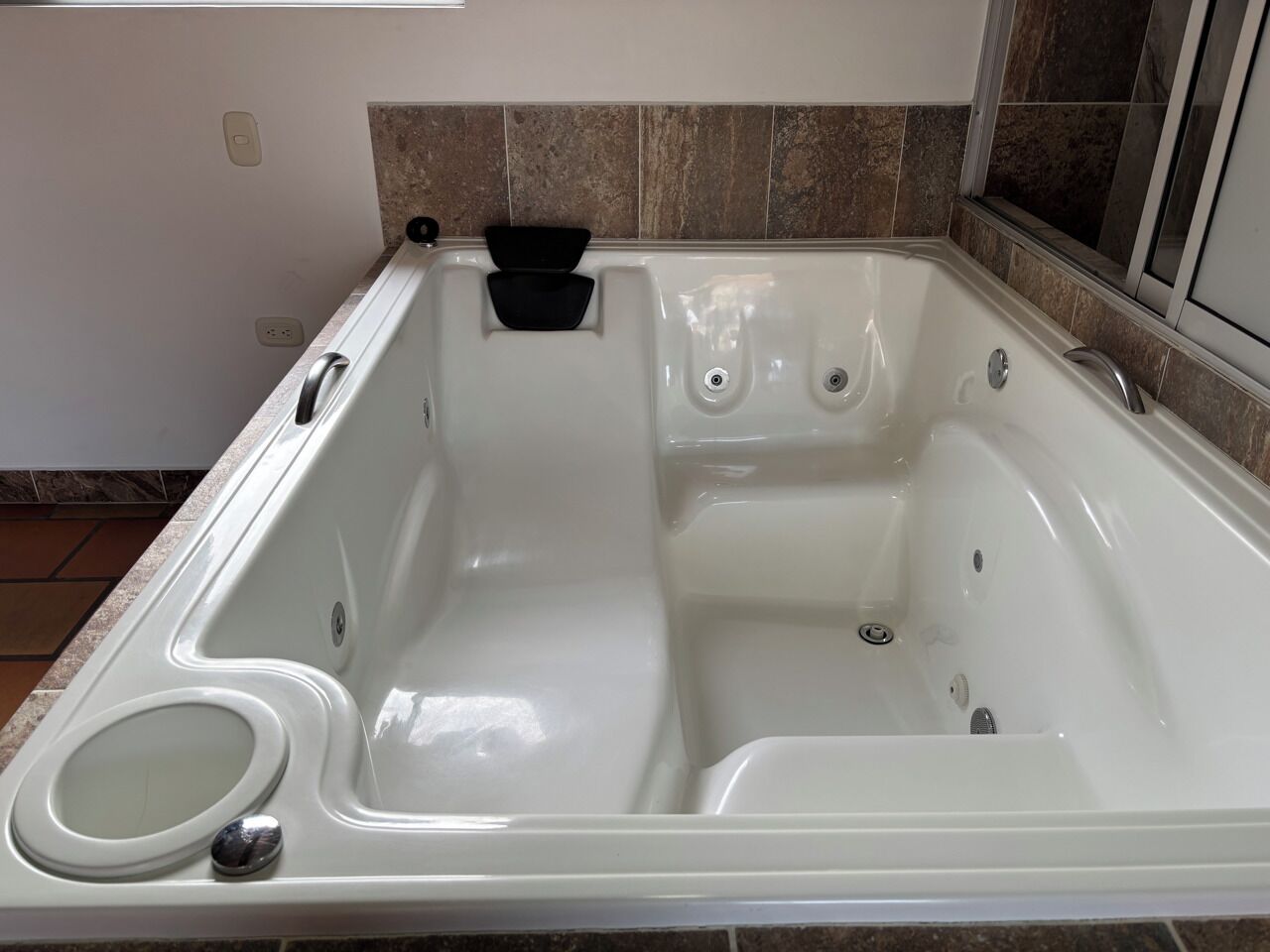 A rectangular hot tub with a built-in seat, a control panel, and a small black object on the edge.
