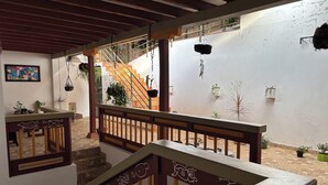 Una scala con ringhiere in legno e fioriere sospese, che conduce a una zona esterna con piante in vaso e vista su un edificio con una scalinata.