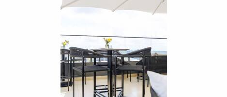 Une terrasse sur le toit avec une table ronde et des chaises, un parasol blanc et une vue sur la mer.