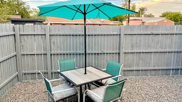 Um pátio com mesa, cadeiras, guarda-sol e cerca de madeira.