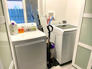 A laundry room with a washing machine, dryer, iron, and ironing board.