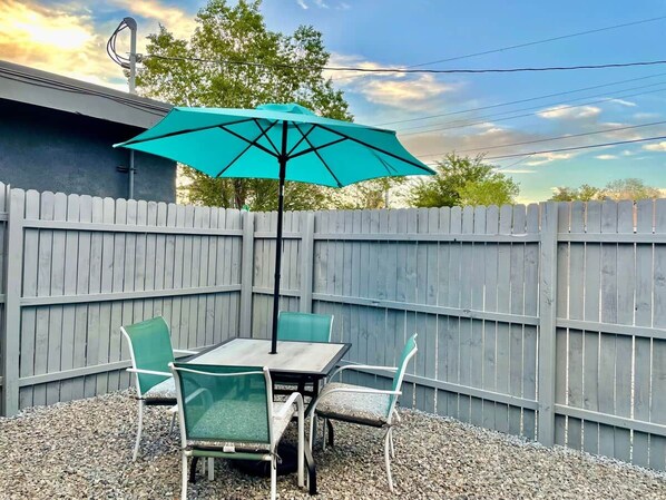 A patio with a table and chairs, a turquoise umbrella, and a wooden fence.