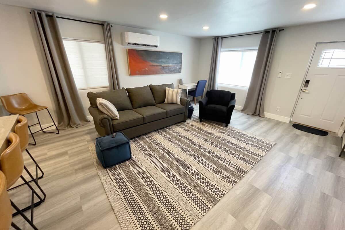 A modern living room with a sofa, armchairs, a dining table, and a patterned rug.