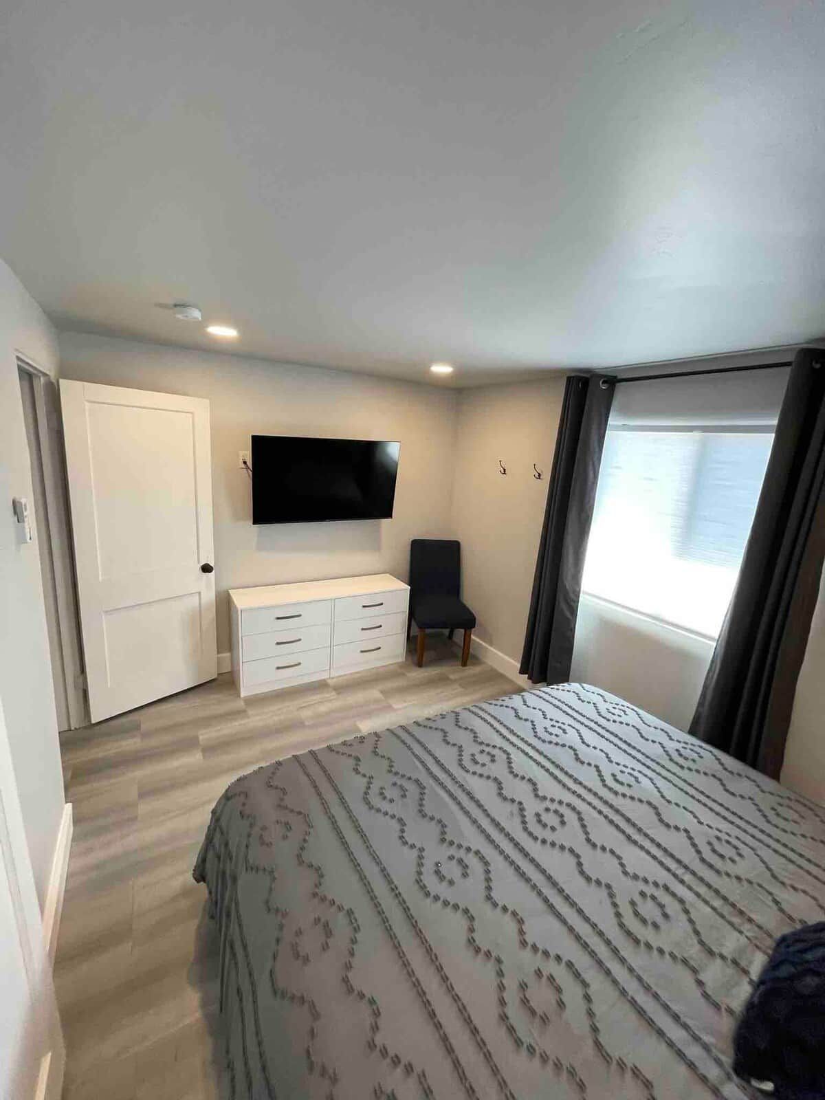 Quarto com cama, televisão, cadeira, guarda-roupa e janela.