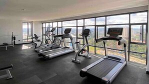 A gym with treadmills, stationary bikes, and a bench. It has large windows and a high ceiling.