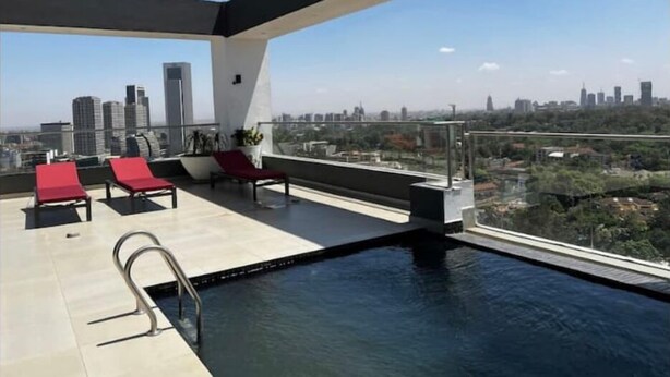 A rooftop pool area with red lounge chairs, a small pool, and a city view.