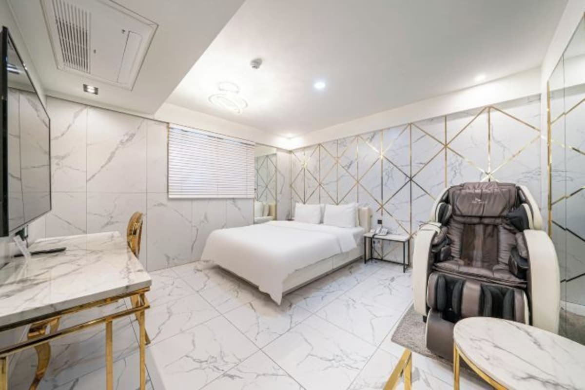 Una habitación de hotel moderna con piso de mármol, una cama, un sillón de masaje, un escritorio y un televisor.