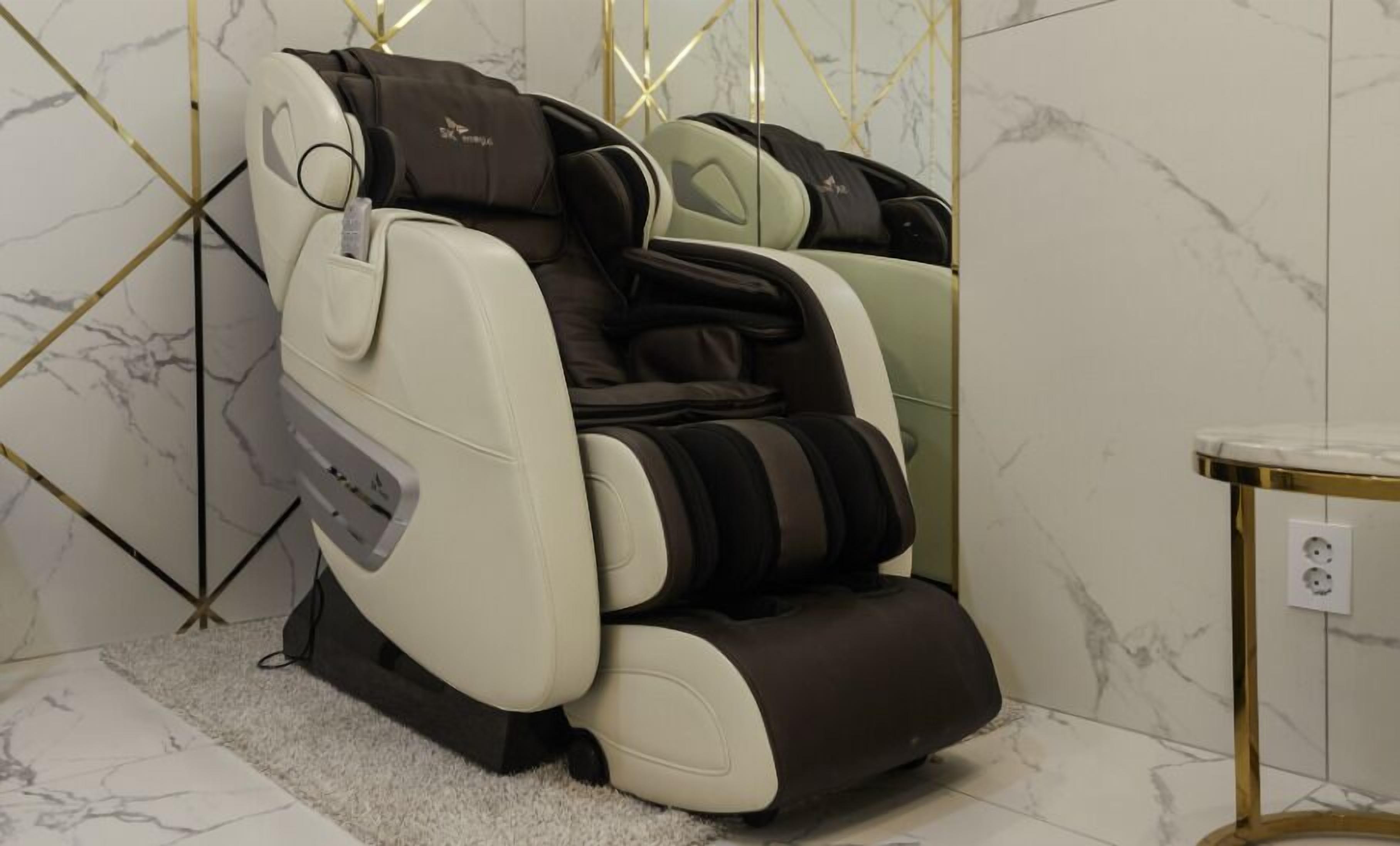 Ein Massagesessel mit Bedienfeld, vor einer Marmorwand mit geometrischen Goldakzenten.