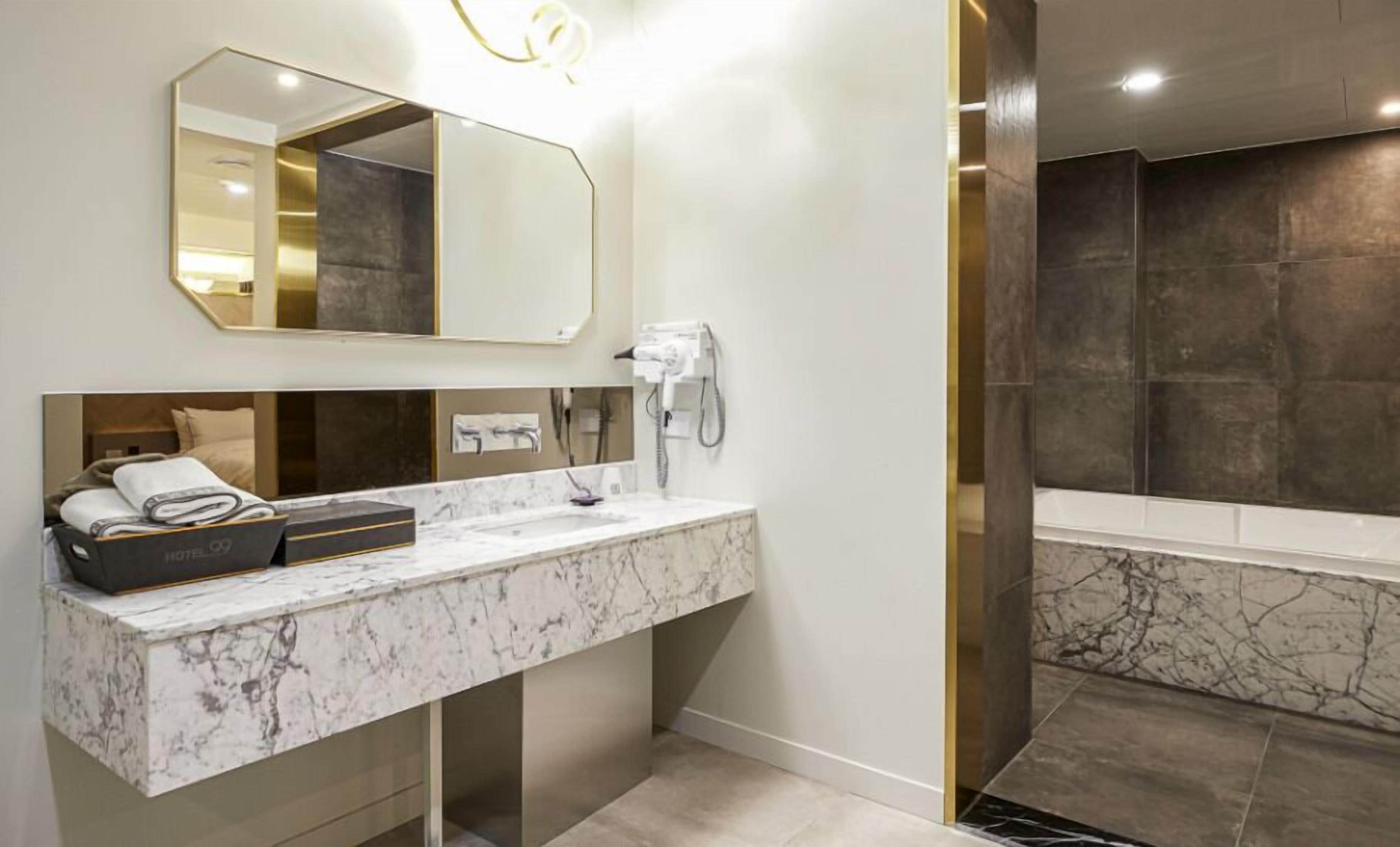 A modern bathroom with a marble sink, a hairdryer, and a large mirror.