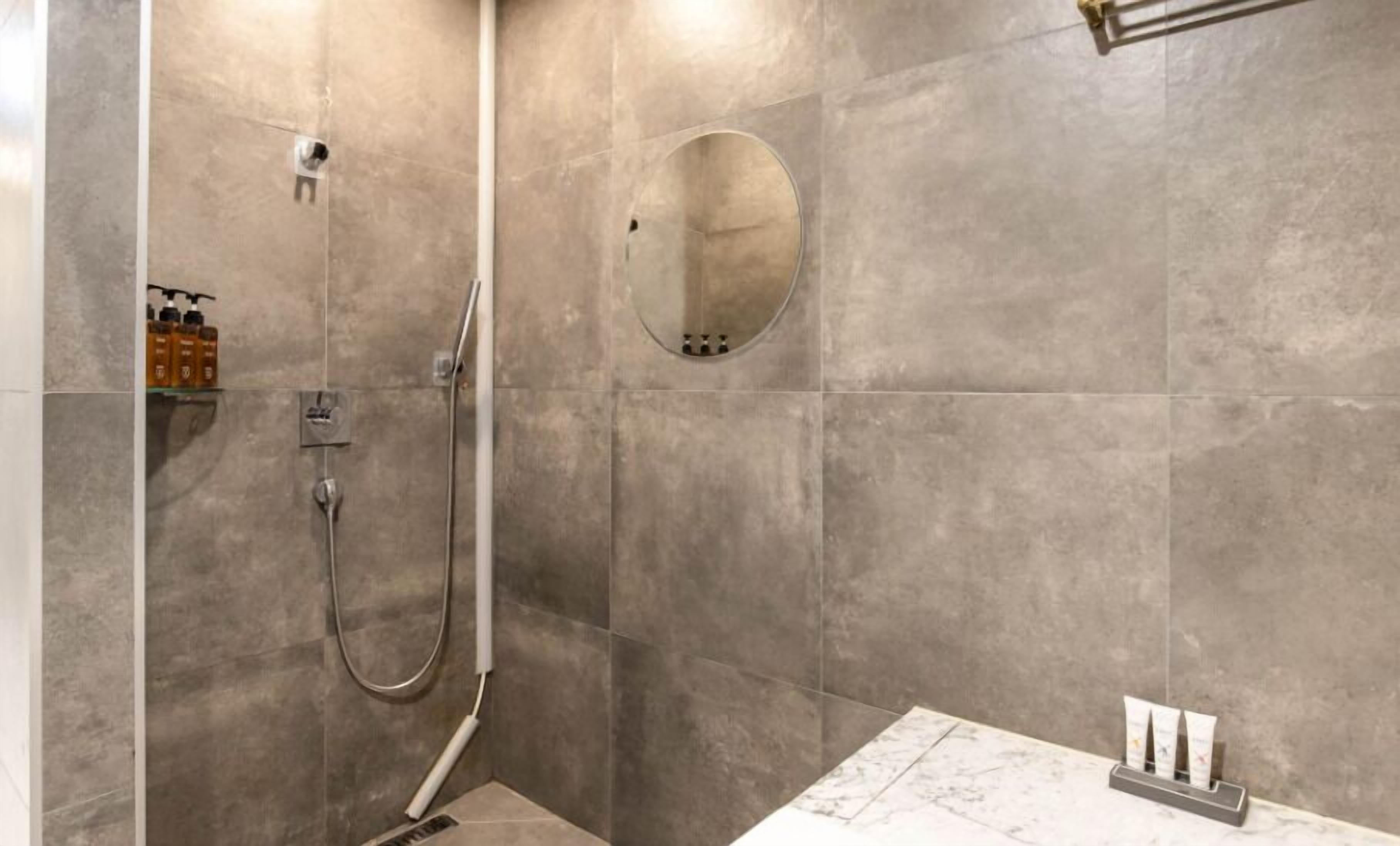 A modern bathroom with a shower, a round mirror, and toiletries on a shelf.