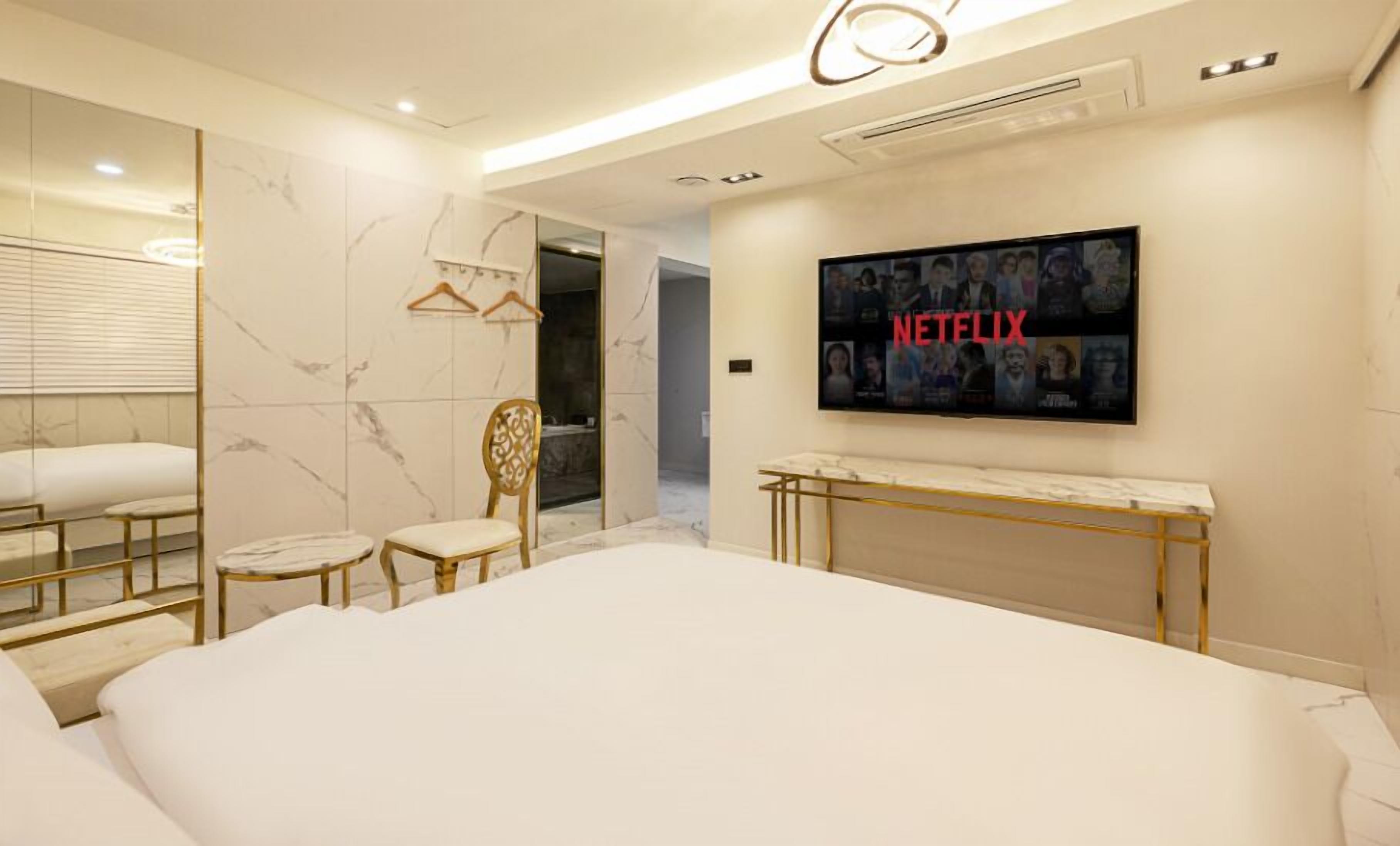 A modern hotel room with a large bed, a TV mounted on the wall, and a mirror with a marble backsplash.