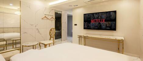 A modern hotel room with a large bed, a TV mounted on the wall, and a mirror with a marble backsplash.